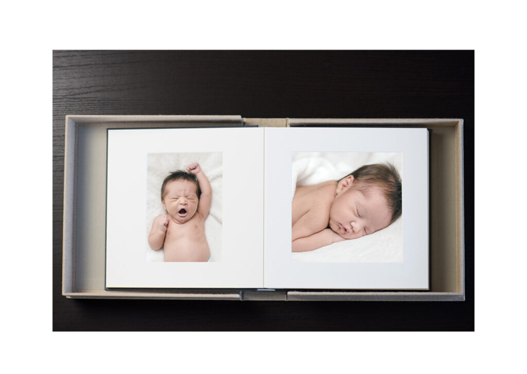 Newborn photo album opened flat by Palo Alto newborn photographer Isela Lozano, showing matted 5x7 prints of a baby yawning and stretching on one side and sleeping on her stomach with her face resting on her hands