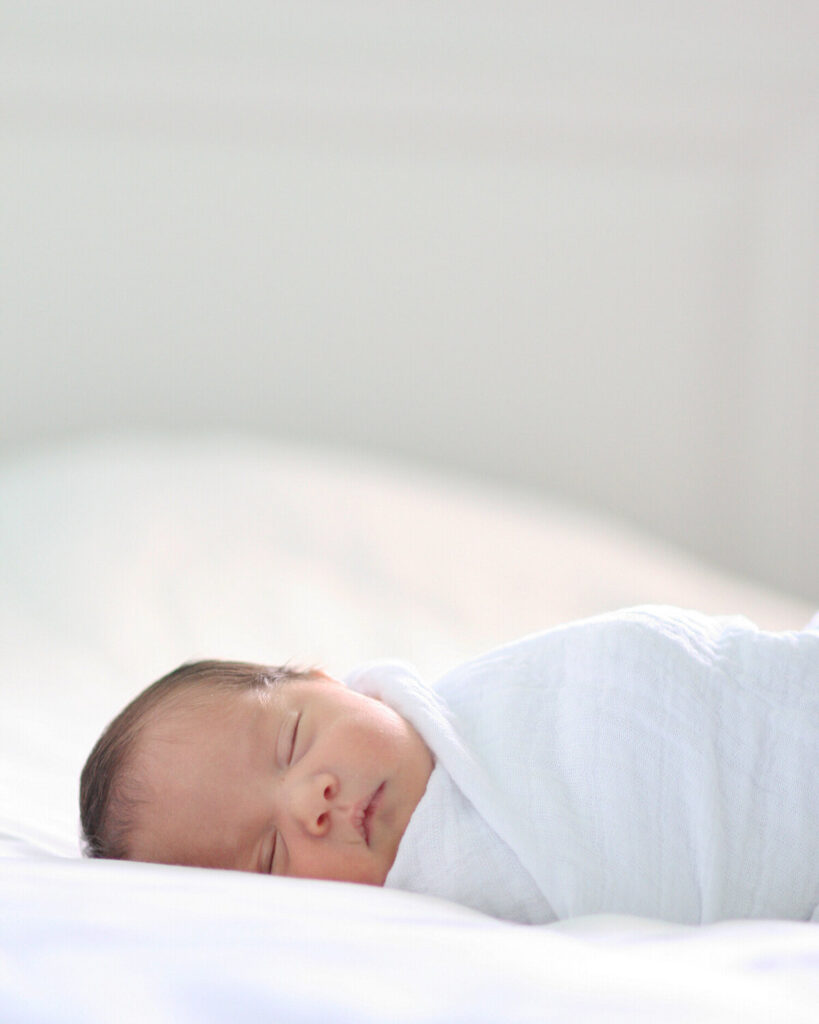 Newborn baby swaddled in white blanket on white bed, natural window light, at-home Mill Valley newborn photography session