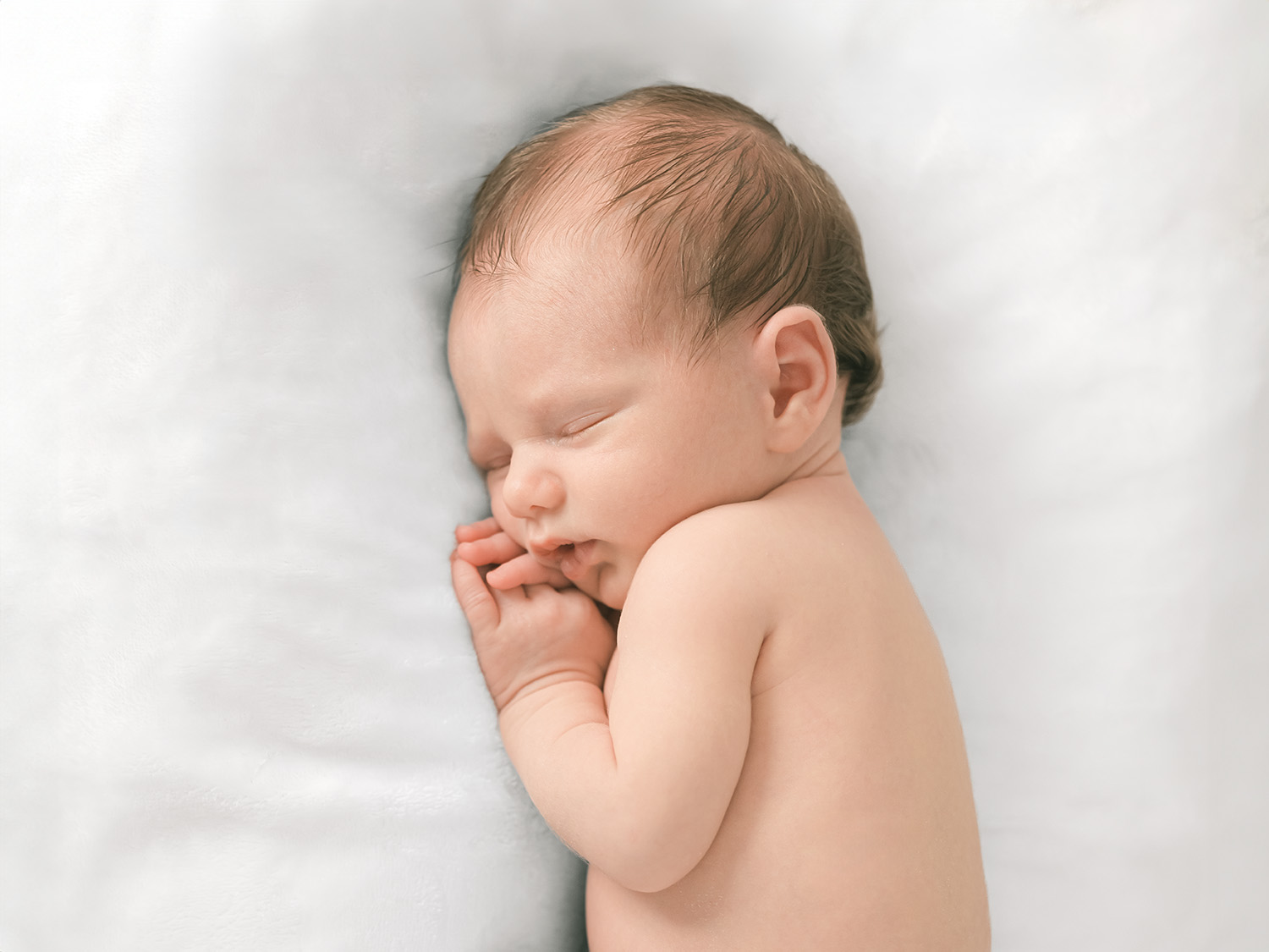 Newborn baby wearing just a diaper sleeping on a white bed, photographed in natural light by a Mill Valley newborn photographer during an in-home session.