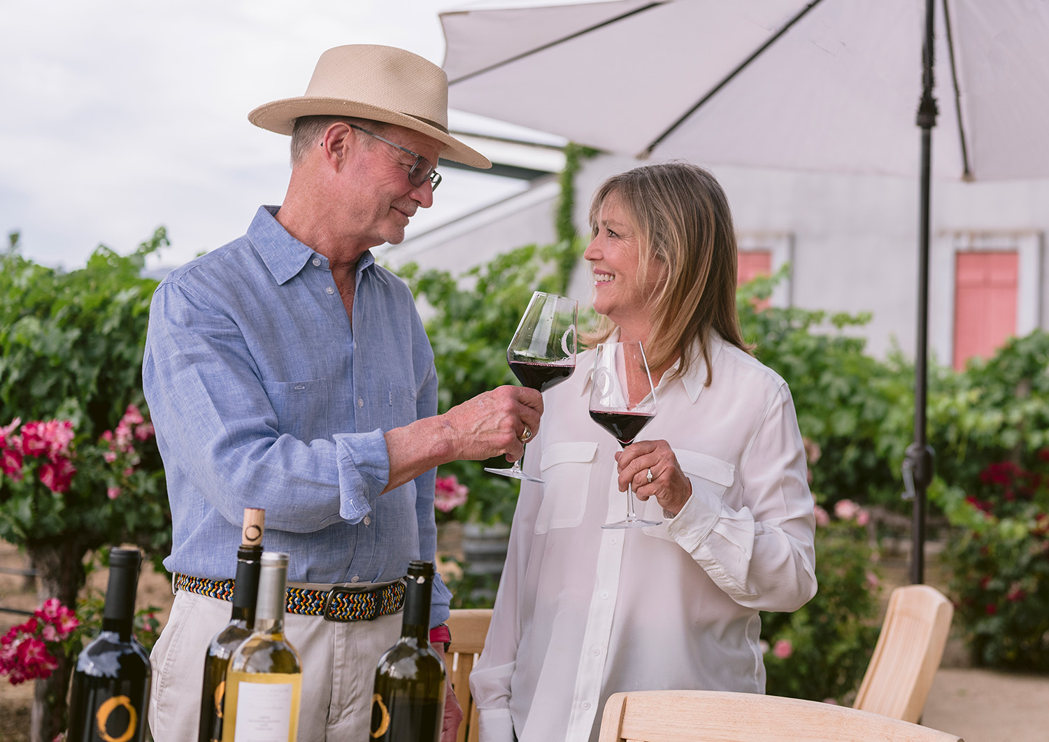 Winery owners at O’Brien Estate in Napa Valley clinking glasses of red wine during a natural light photography session in the vineyard.