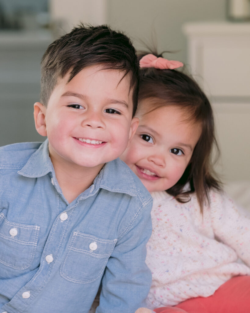 Toddler brother and toddler sister leaning in towards each other smiling at the camera in their Palo Alto home