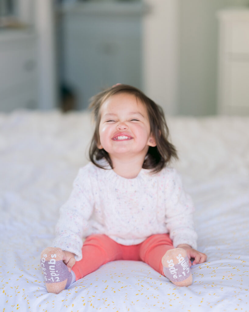 Close-up of toddler girl grinning on the bed in soft natural light