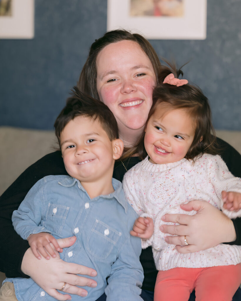 Mom hugging her two toddlers on a cozy couch during an in-home family session in Palo Alto