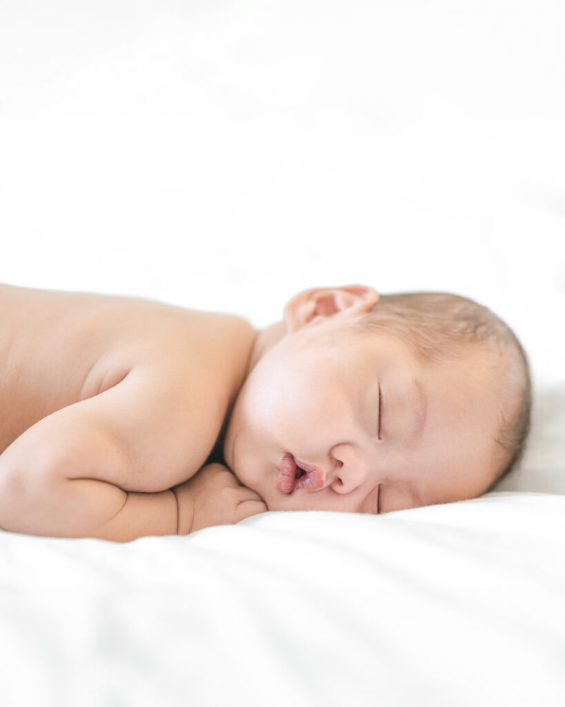 Newborn baby sleeping on stomach in diapers with hands tucked under chin, bathed in bright natural light, photographed by Palo Alto newborn photographer.