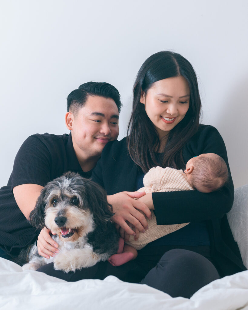 Family with newborn baby and dog on bed.