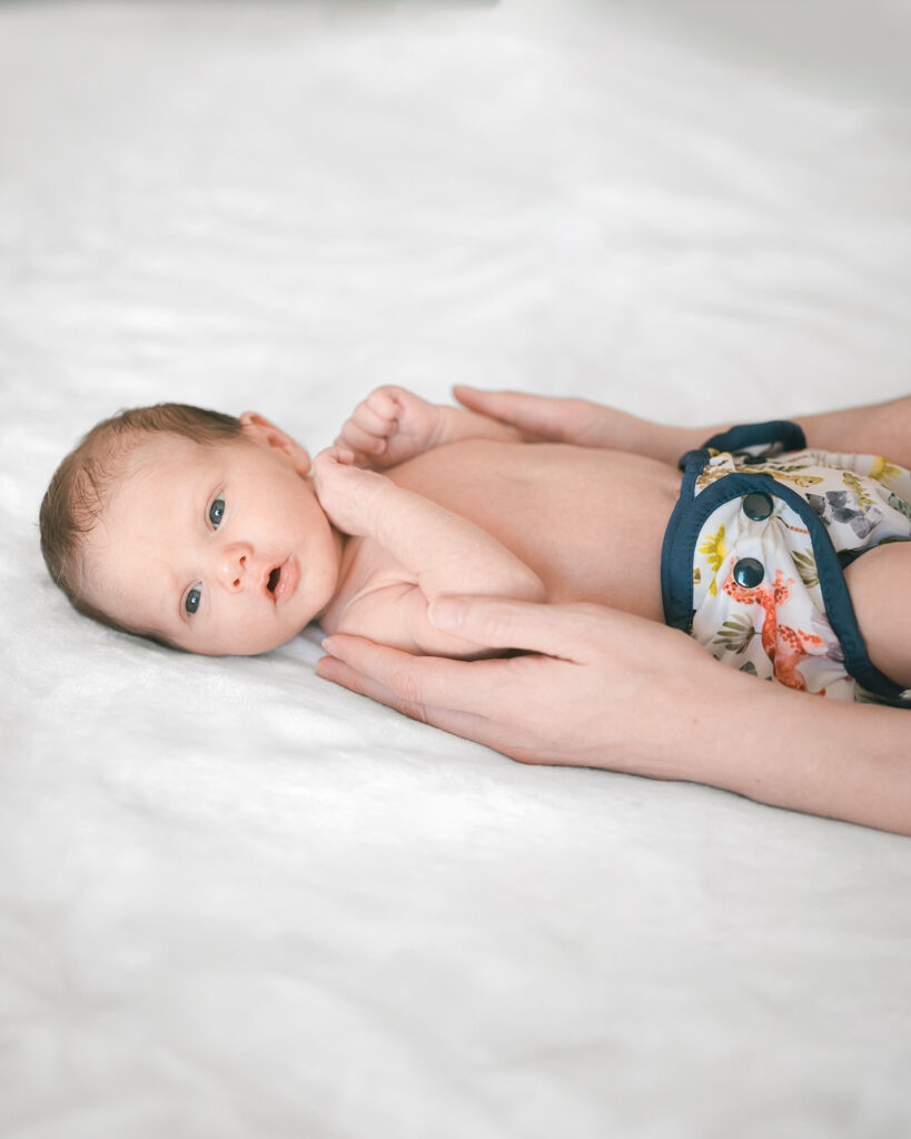 Newborn baby boy wearing disposable diapers laying on bed during an in-home photography session by Palo Alto newborn photographer, Isela Lozano.