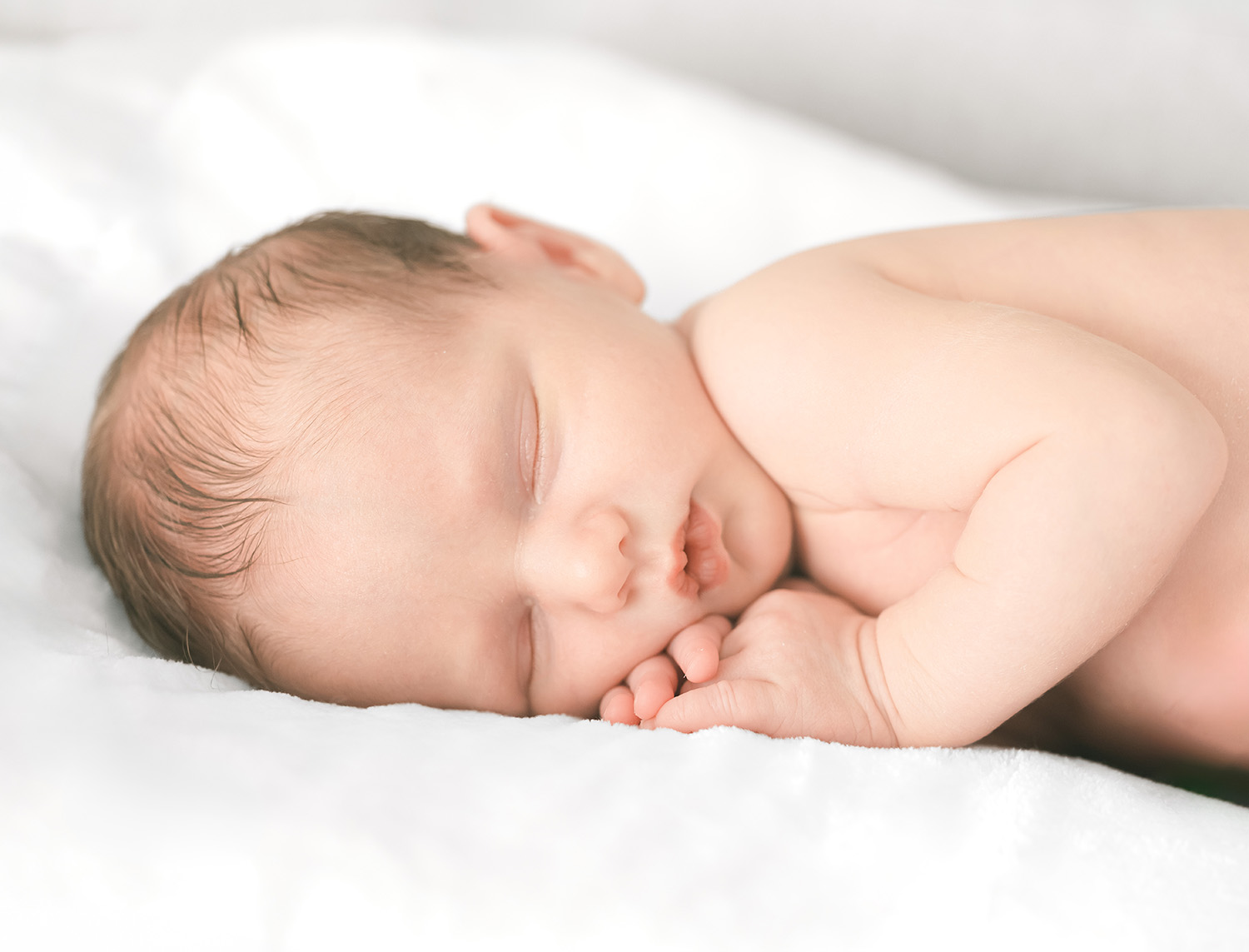 Palo Alto newborn photographer in-home lifestyle session using natural light, tight shot of a sleeping newborn resting on their stomach with hands tucked under their chin.