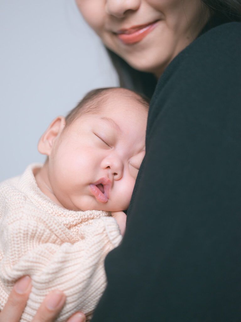 Newborn baby held close to mother’s chest as she smiles, intimate moment captured by Palo Alto newborn photographer.