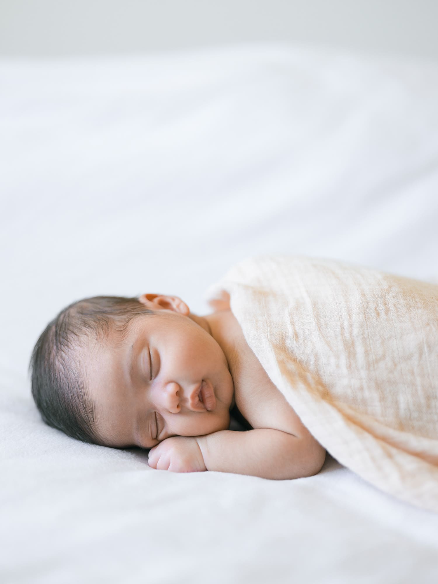 Close-up photo of a shirtless baby girl sleeping on her tummy with her hand under her chin, covered by a light yellow blanket on a white bed, by an SF Marina District in-home newborn photographer.